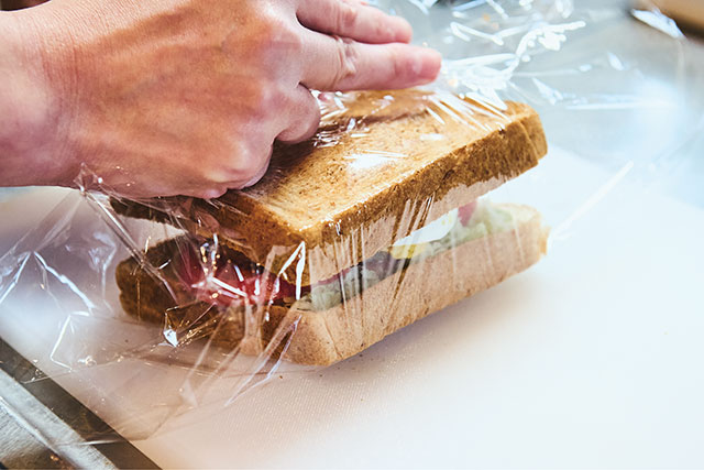 １枚のパンにキャベツ、トマト、サラダチキン、ゆで卵の順にのせ、もう１枚で挟む。ラップできつめに全体を包む