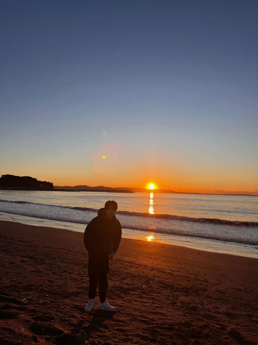 日の出の海の前に立つ稲井孝太朗